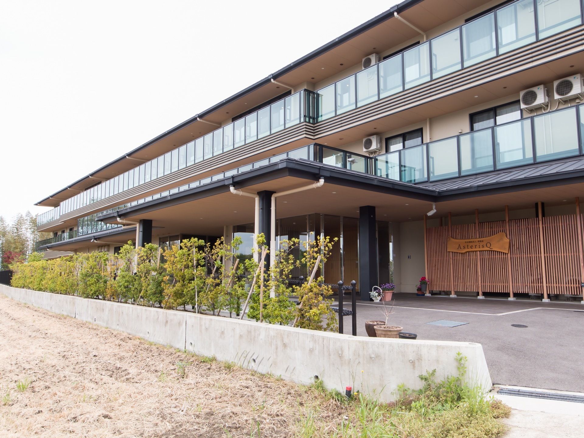 幅広い外観で、植栽を設けた３階建ての施設である。各居室にはエアコンやベランダが完備され、見通しの良いフェンスが設置されている。