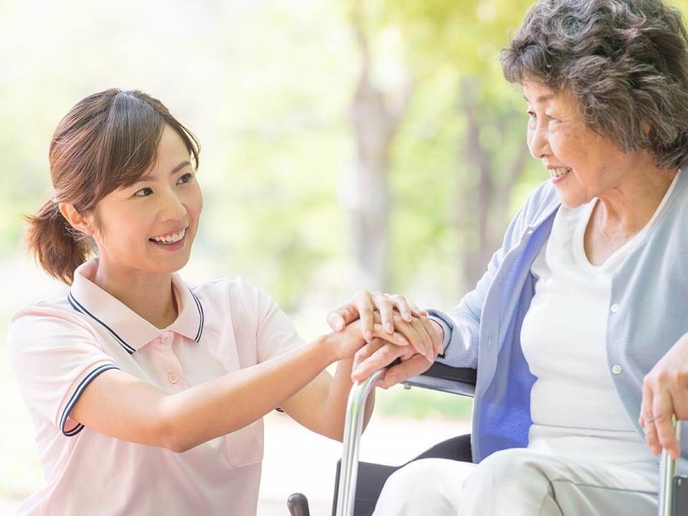 車いすの女性と同じ視線で話している介護スタッフ。やわらかい表情で散歩している様子