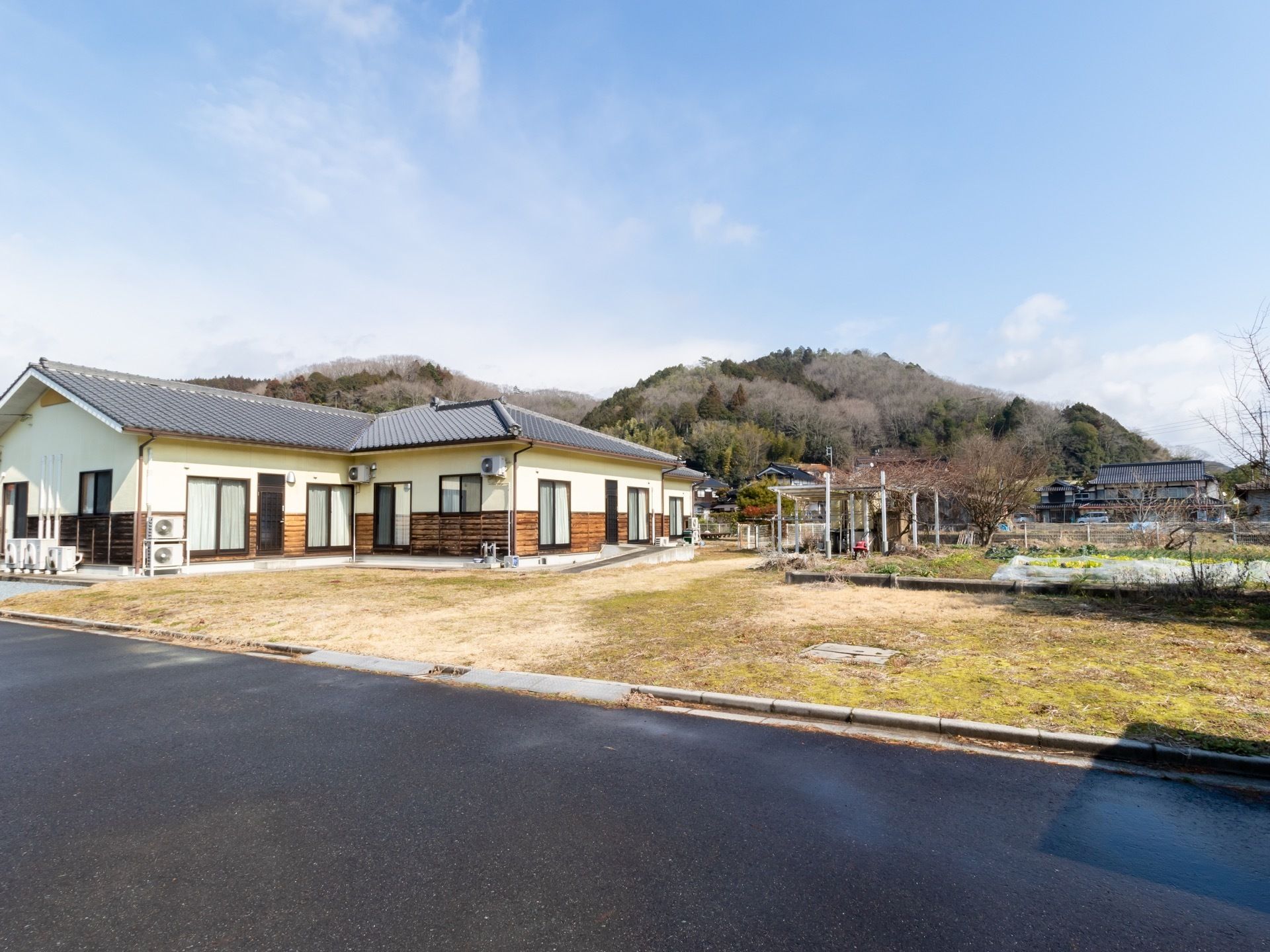 自然に囲まれた場所に位置する施設である。民家が付近にあり、手前には畑も見える。建物は平屋建てとなっている。
