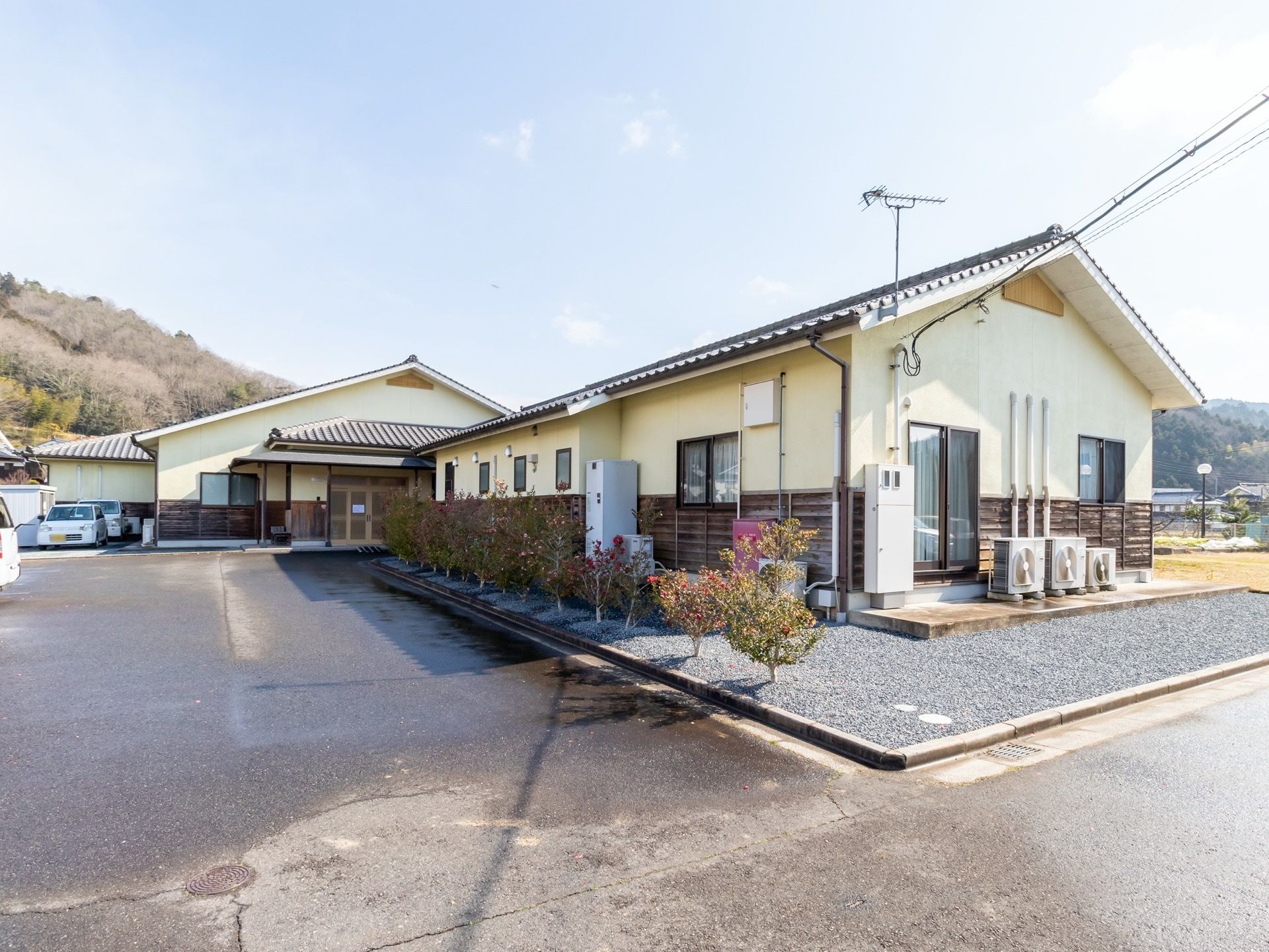 建物の奥には複数の山が見え、自然に囲まれた高い建物がない場所である。建物の前には広いスペースがある。