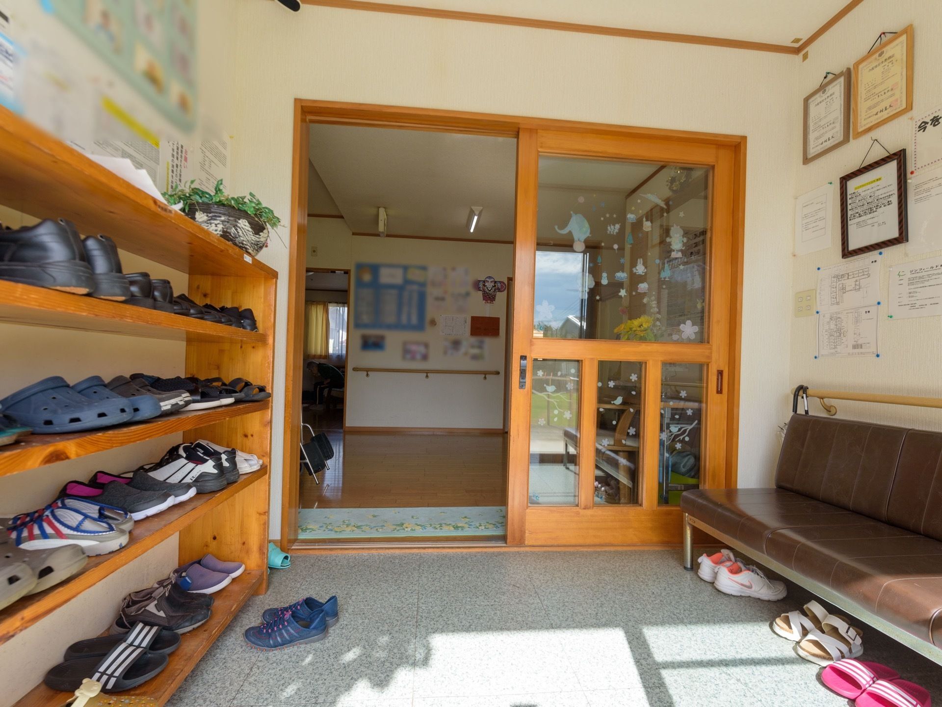 大きなガラスの引き戸が正面にあり、ガラス戸の手前には大きな下駄箱と、ベンチが設置されている。下駄箱の中にはたくさんの靴が収納されている。