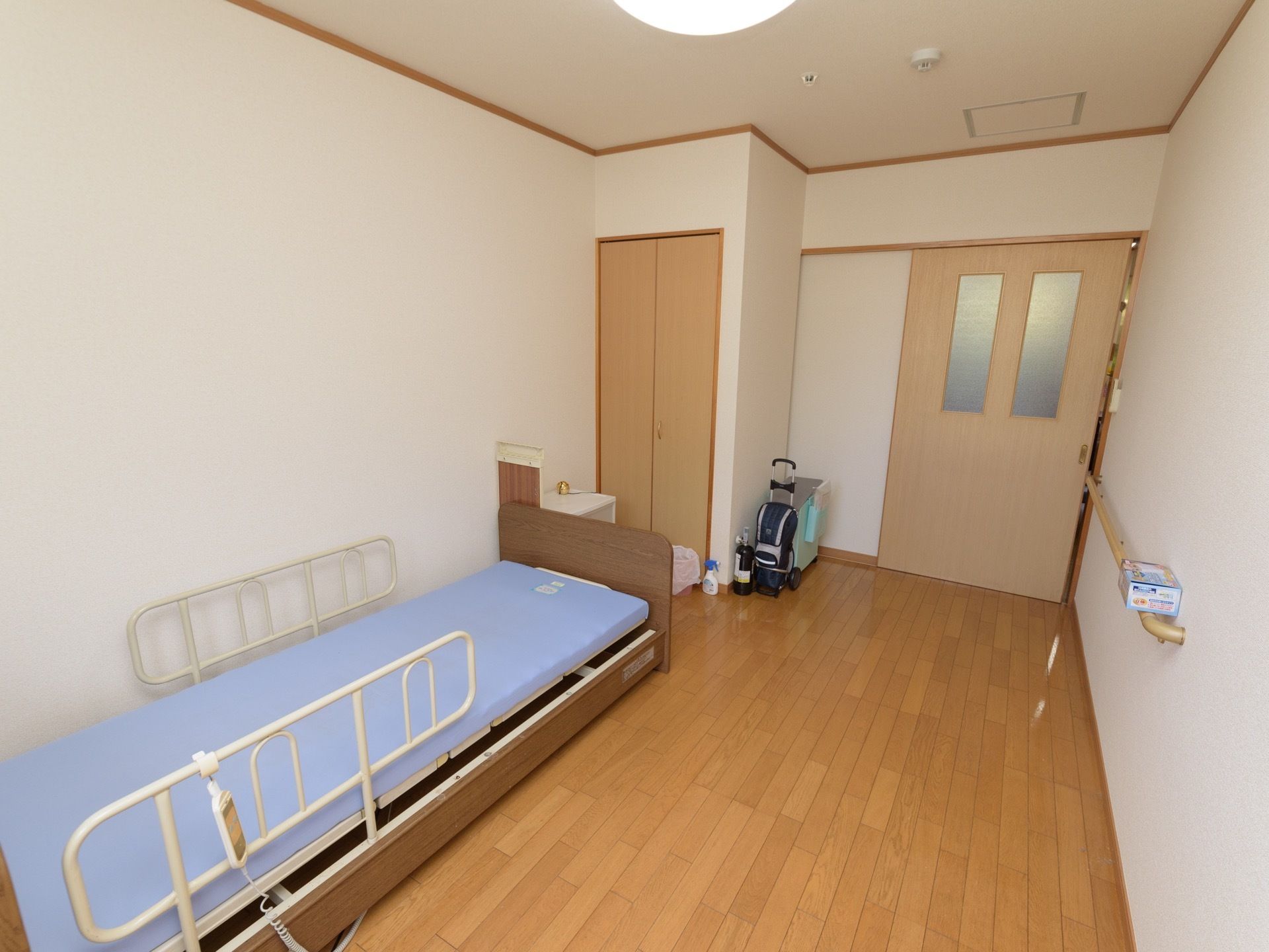居室の扉は引き戸になっていて、室内の壁には手すりが備え付けられている。作り付けの収納があり、介護用ベッドも設置されているのが見える。