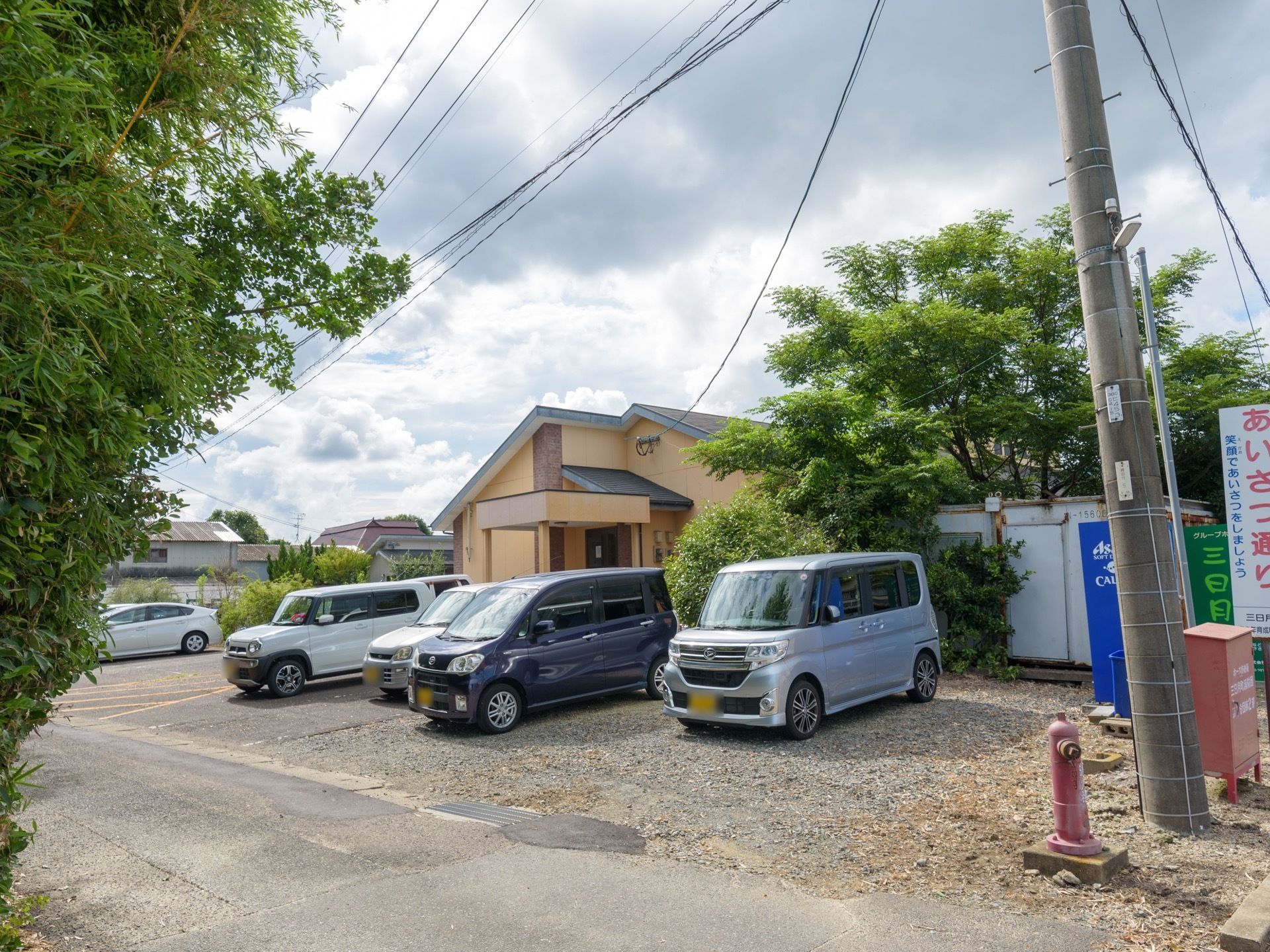 道路に面した駐車場があり、複数の自動車が駐車されている。駐車場の奥にはホームの建物があるのが見える。