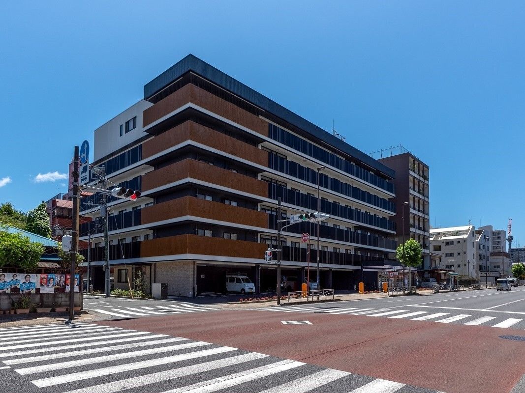5階建ての建物はブラウンとグレーでまとめられ、各フロアにベランダが付いている。日当たりのいい場所に建っている。
