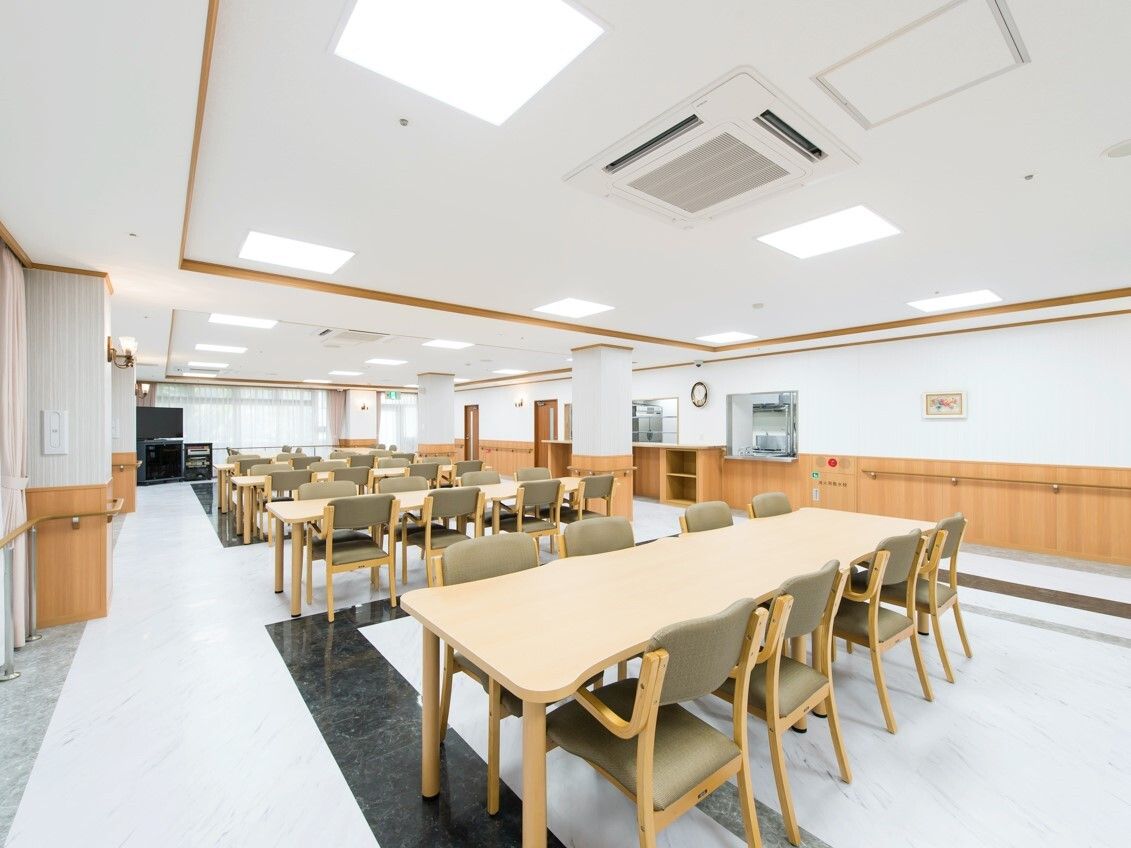 大きなテレビが窓際に設置され、木製の大きなダイニングテーブルセットが複数置かれた食堂。