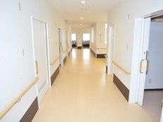 まっすぐな廊下の両サイドに手すりと居室があり、木製の手すりが全域に付いている。居室のドアはスライド式で、幅が広いタイプ。