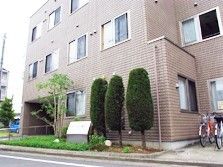 3階建てのブラウン系の建物の周りには木が植えられ、駐輪スペースもあり、一般の賃貸物件のような雰囲気。