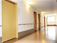 手すりが付いたまっすぐな廊下。奥にはカーテン付きの窓があり、居室には引き戸が付いている。