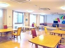 木製のテーブルが複数並ぶ明るい雰囲気の共有スペースにはテレビもあり、壁には虹の絵が描かれている。