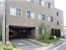 建物の１階部分には駐車スペースがあり、車いすのマークが描かれている。周囲には木も植えられナチュラルな雰囲気。