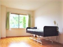 カーテンが付いた居室はフローリングで、緊急通報装置が窓際に付いたベッドが置かれている。