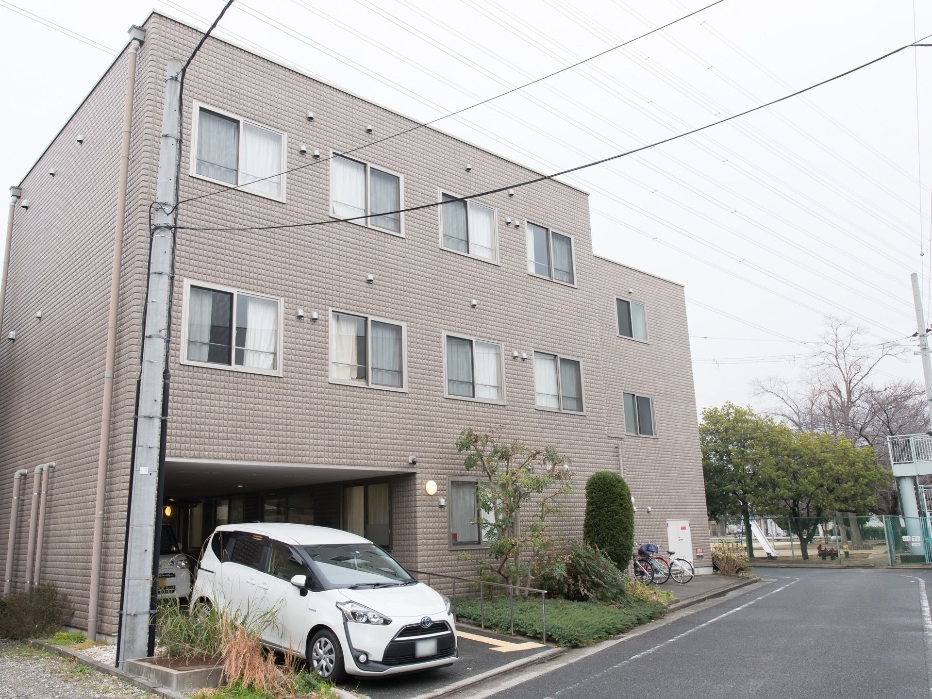歩道橋やすべり台のある公園のそばに立地する3階建ての施設である。植え込みや駐車スペースを完備している。