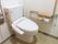 温水洗浄便座が完備されたトイレである。壁には、カウンター付きのL字型手すりや呼び出しブザーが設置されている。