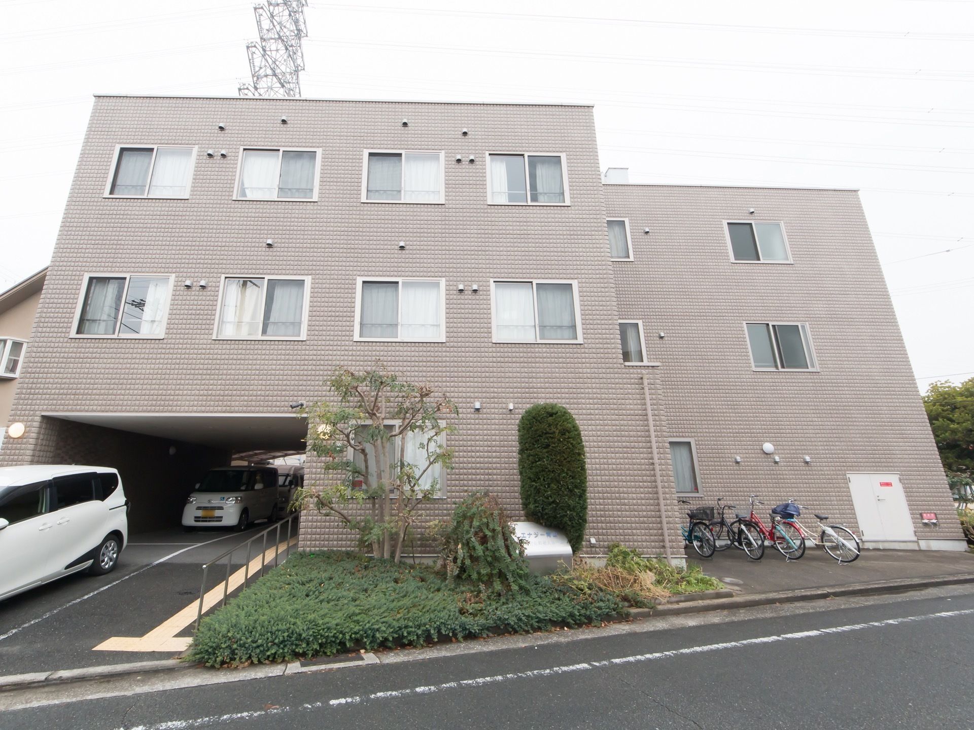 三角地形に立地する3階建ての施設である。前面中央部に植え込みを設け、両サイドに駐車スペースと駐輪スペースを分けて設けている。