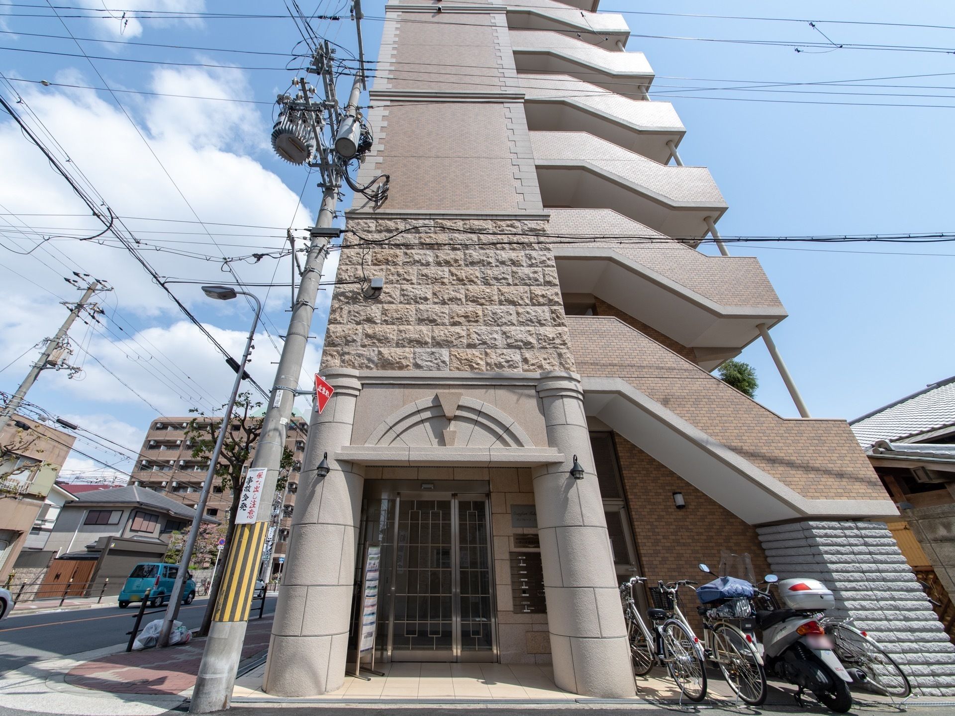 施設は道路の角地に建つ７階建ての建物である。１階に入口があり、郵便受けが設置されている。入口横には自転車が数台とめてある。