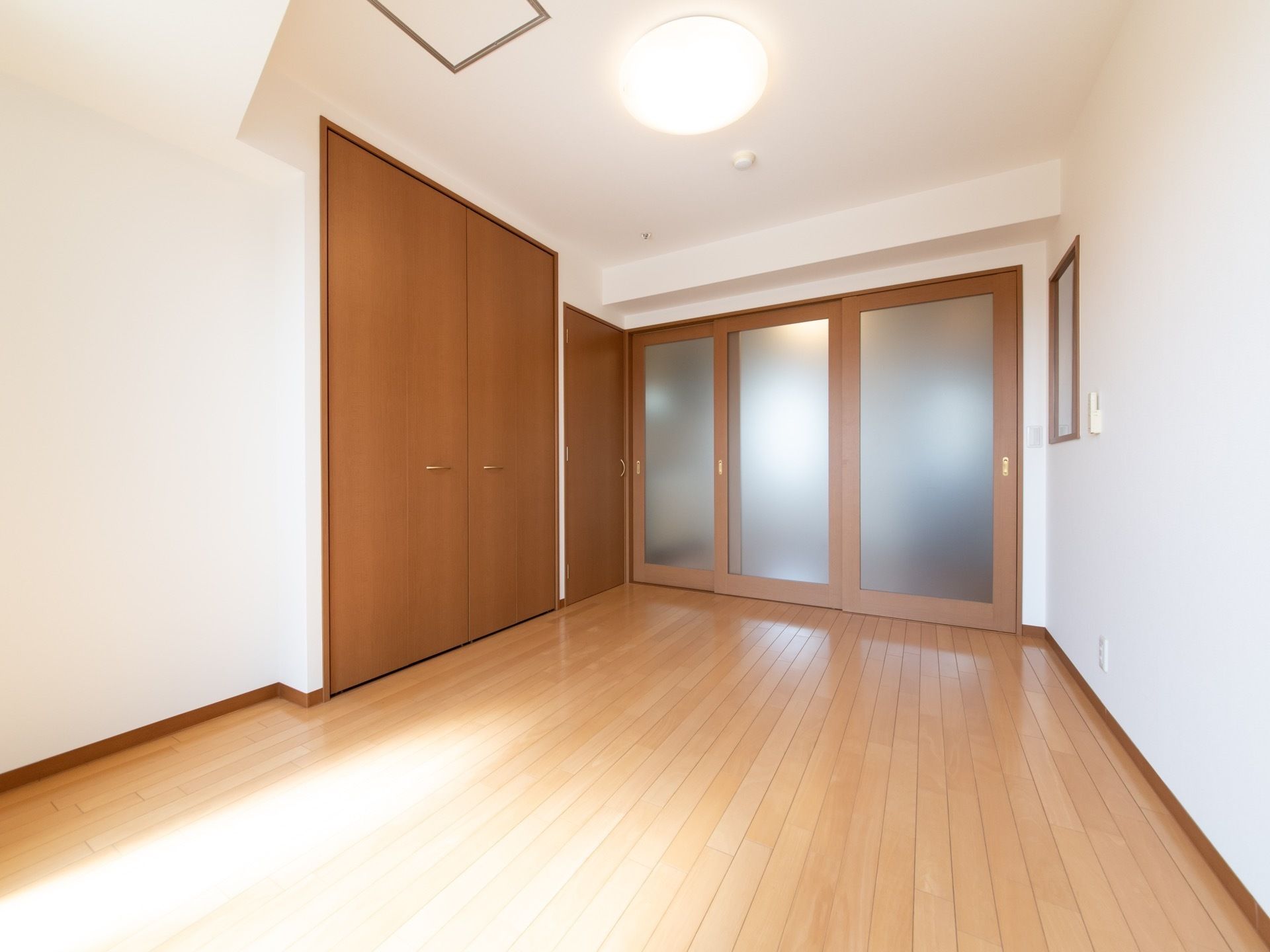 窓側の奥の部屋は光がよく入り明るい。茶色い大きなクローゼットが設置されている。照明は丸いシーリングライトである。