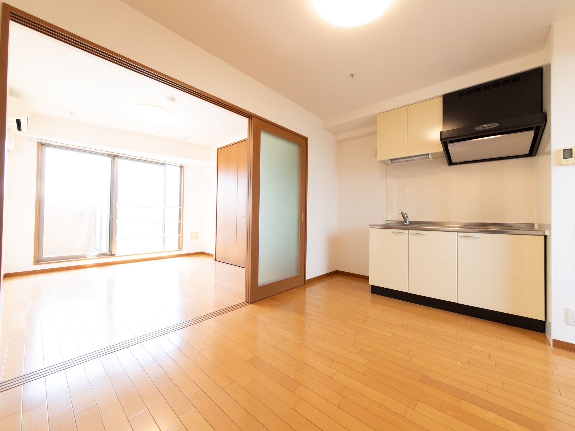 手前の部屋にはキッチンがある。流しとＩＨコンロが横に並んでおり、上と下には白い開き戸の戸棚がある。冷蔵庫を置くスペースもある。