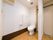 白い壁とフローリングが明るい雰囲気のトイレの扉はカーテン式になっている。便器の横の壁にはL字型に手すりが設置されている。