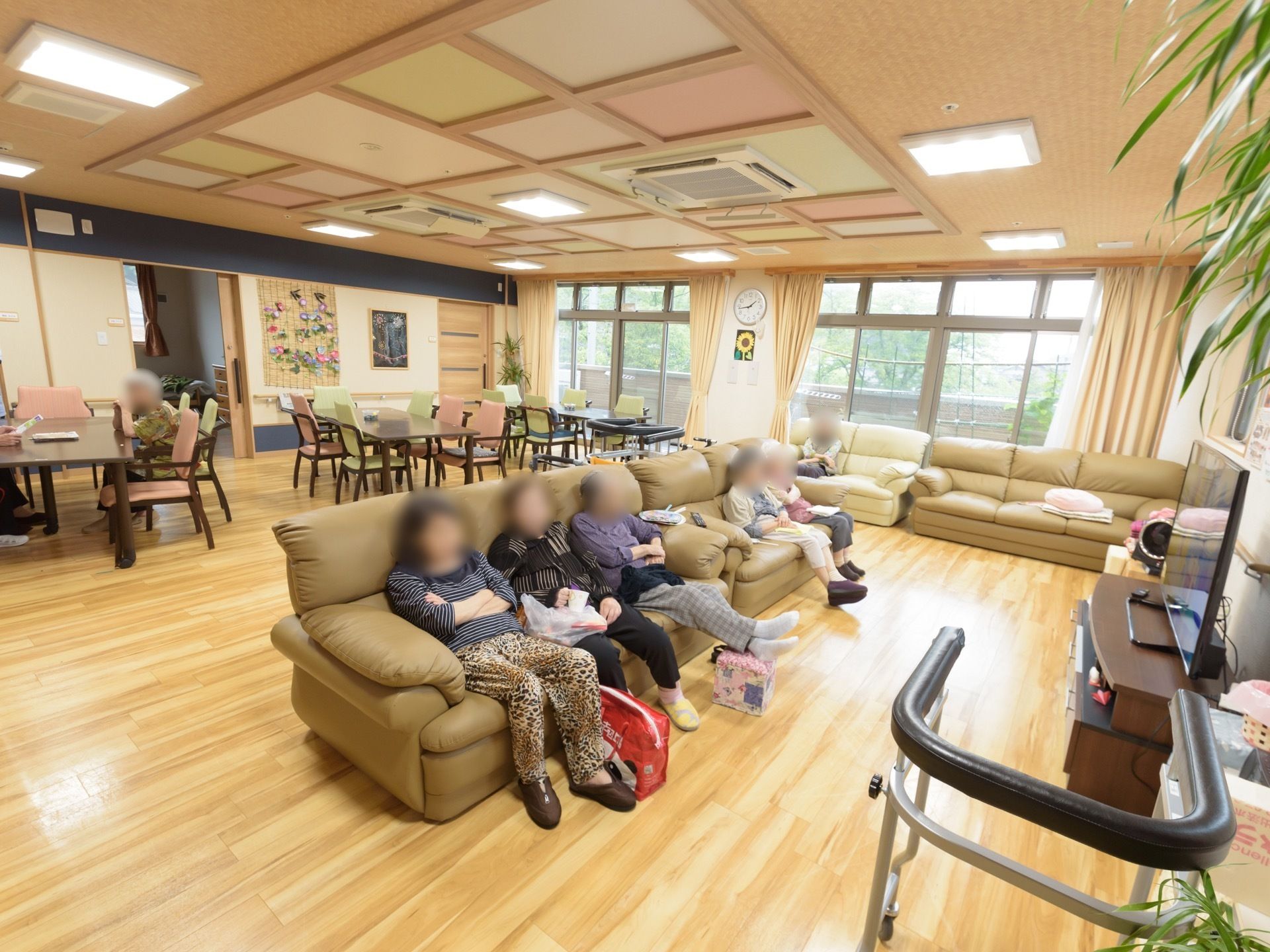 掃出し窓が連なった広い部屋である。床は淡い色のフローリングであり、テーブルセットのエリアと、ソファセットのエリアがある。