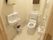 背もたれのある、温水洗浄便座の洋式トイレである。手前の壁に手洗い器があり、反対側の壁にペーパーホルダーがある。