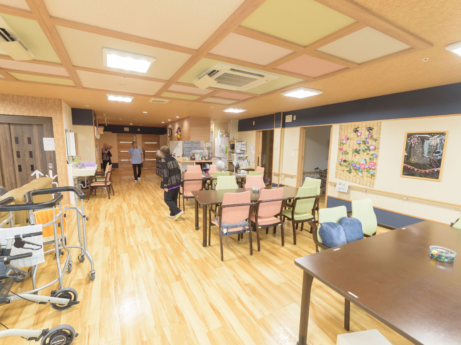 大きなテーブルと椅子が３セット並んでおり、左側には歩行補助の機械が置いてある室内