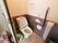 洋式トイレには温水洗浄便座が取り付けられている。トイレの扉は横開きになっている。トイレ内には暖色の電球が灯っている。