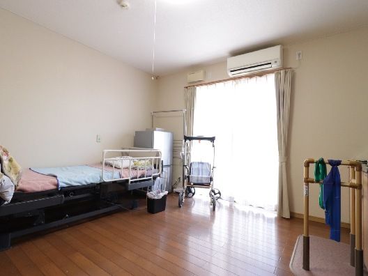 エアコンが付いたフローリングの部屋には寝具付きのベッドがあり、大きな窓にはカーテンが付いている。