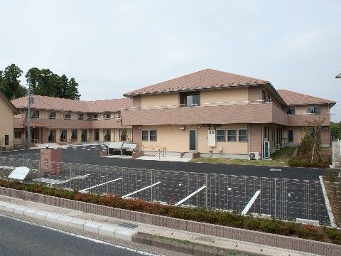 低い位置の植え込みとフェンス越しに駐車場が完備されている施設外観