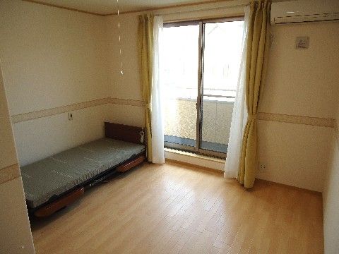 明るい木目調のフローリングに未使用の介護用ベッドが置かれたご入居前の居室
