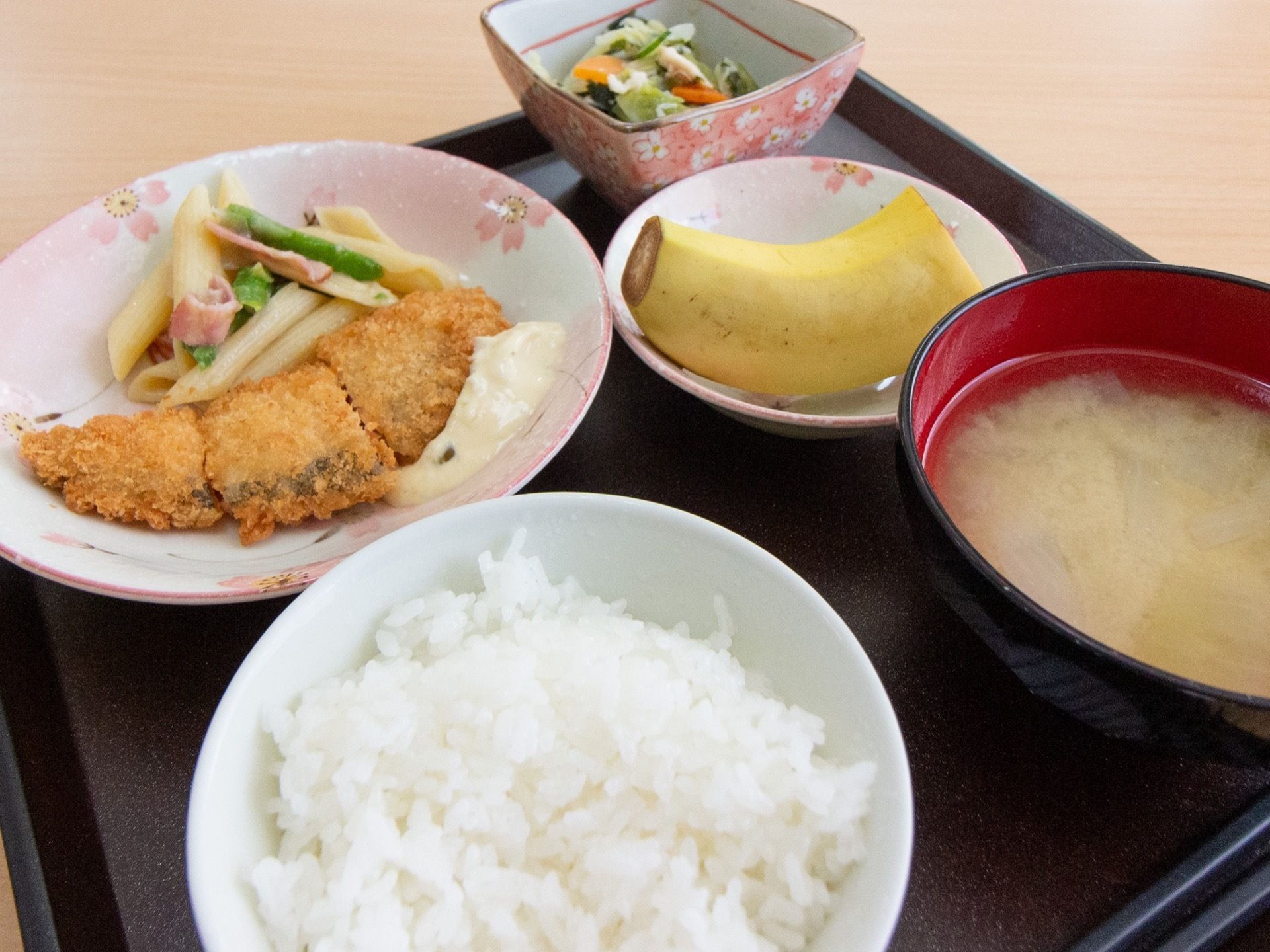 ある日の米飯、味噌汁、メイン、小鉢、フルーツの食事内容である。彩りよく、食器も華やかなものを使用している。