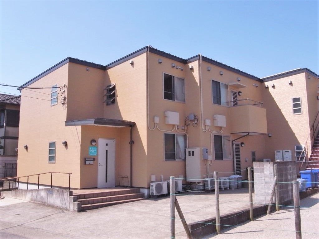 2階建ての建物はブラウン系で玄関前にスロープと階段が、また屋外に避難用の階段もある。