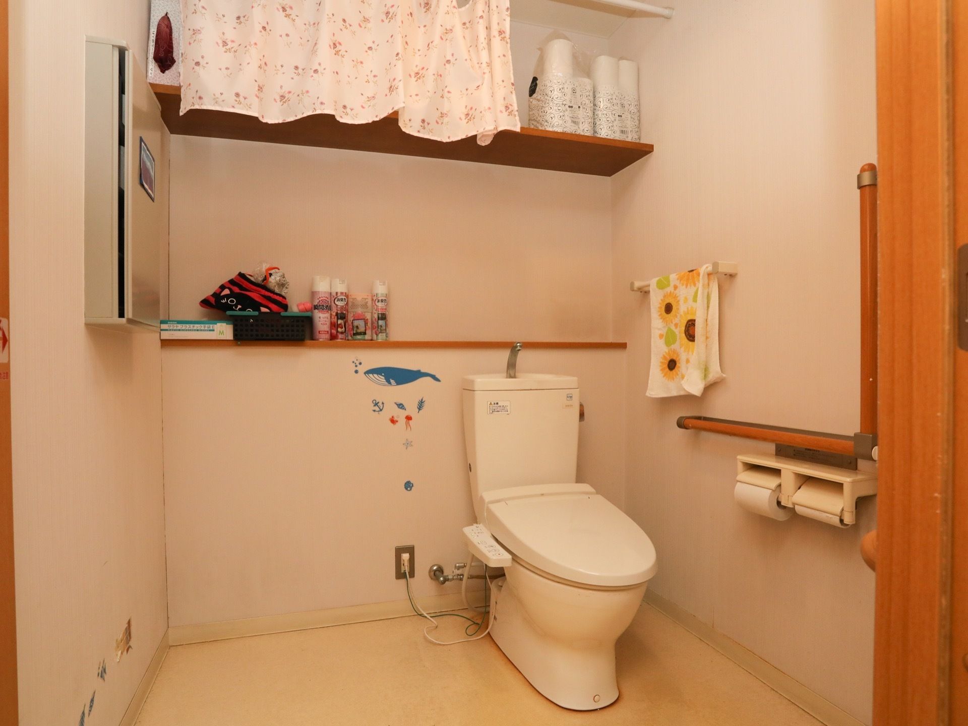 トイレには温水洗浄便座が設置されており、便座の後ろには棚がある。棚にはトイレットペーパーや消臭剤が置かれている。