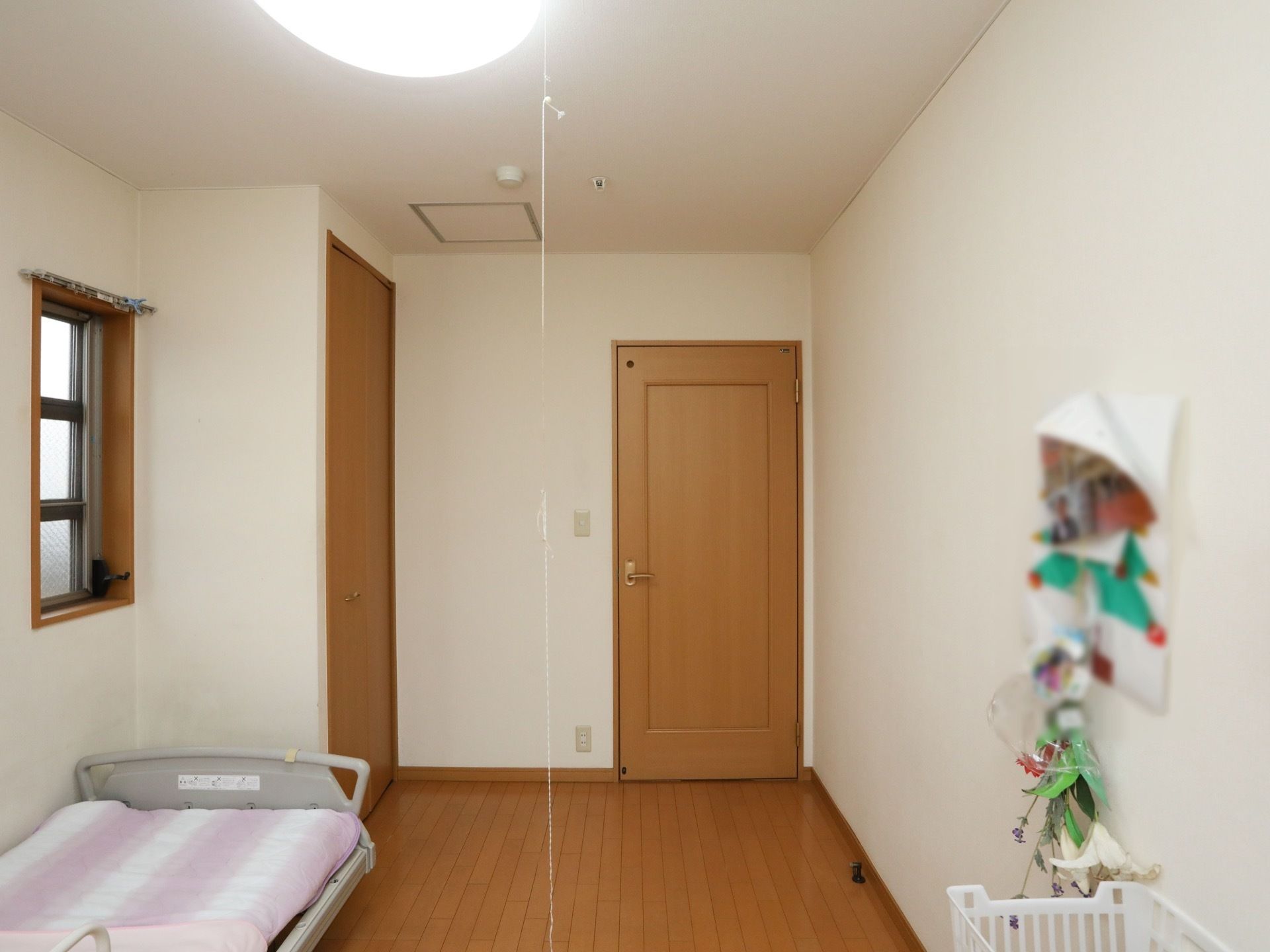 白い壁に木目調のドアが設置された居室。床はフローリングで、介護用ベッドがある。クローゼットが備わっている。