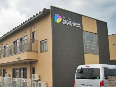 2階建ての建物はベージュとグレーで、ベランダが付き、外壁にはホーム名が書かれている。