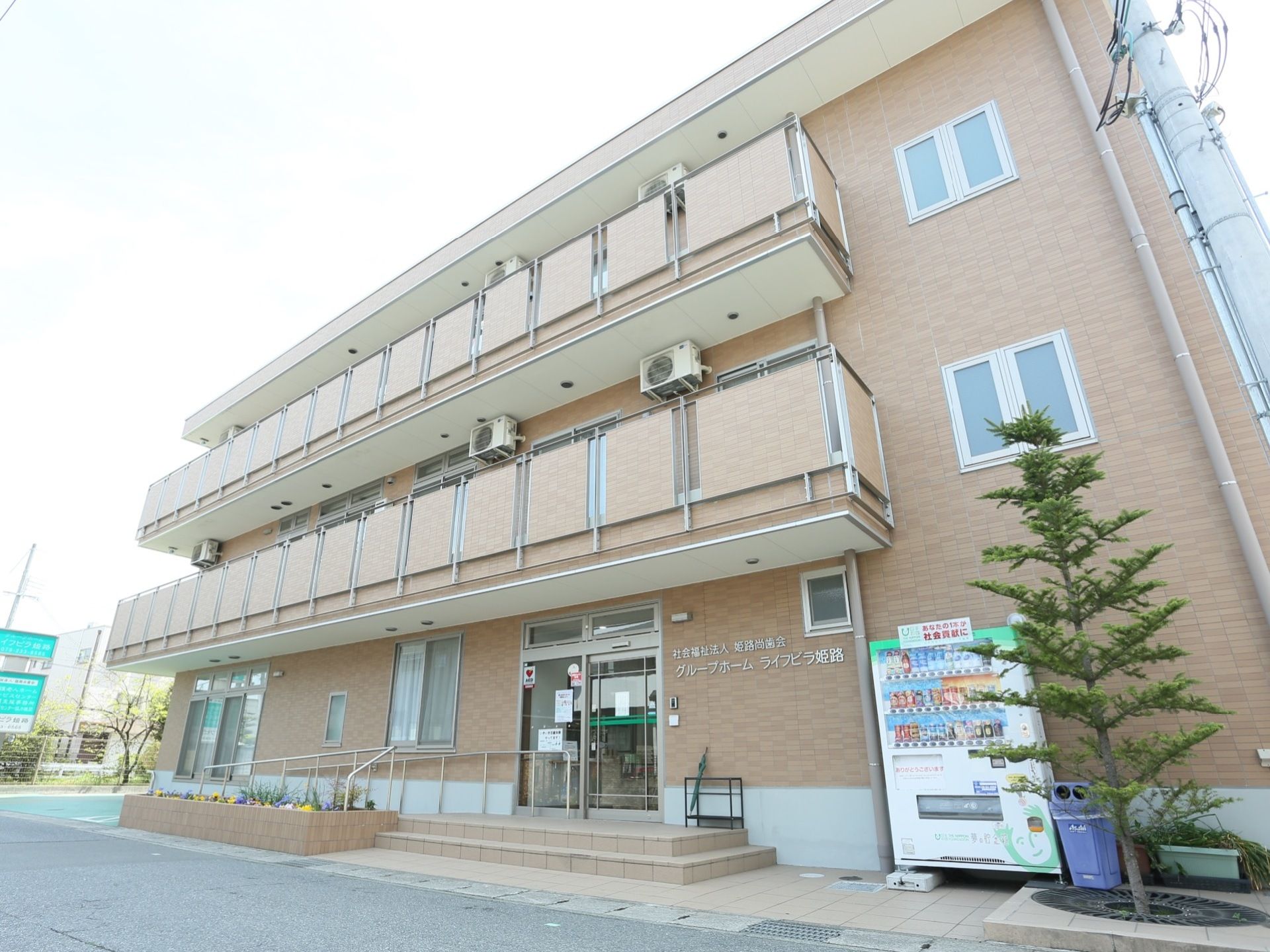 ３階建てのマンションのような施設外観である。外には自動販売機が設置されている。手すり付きのスロープが用意されている。