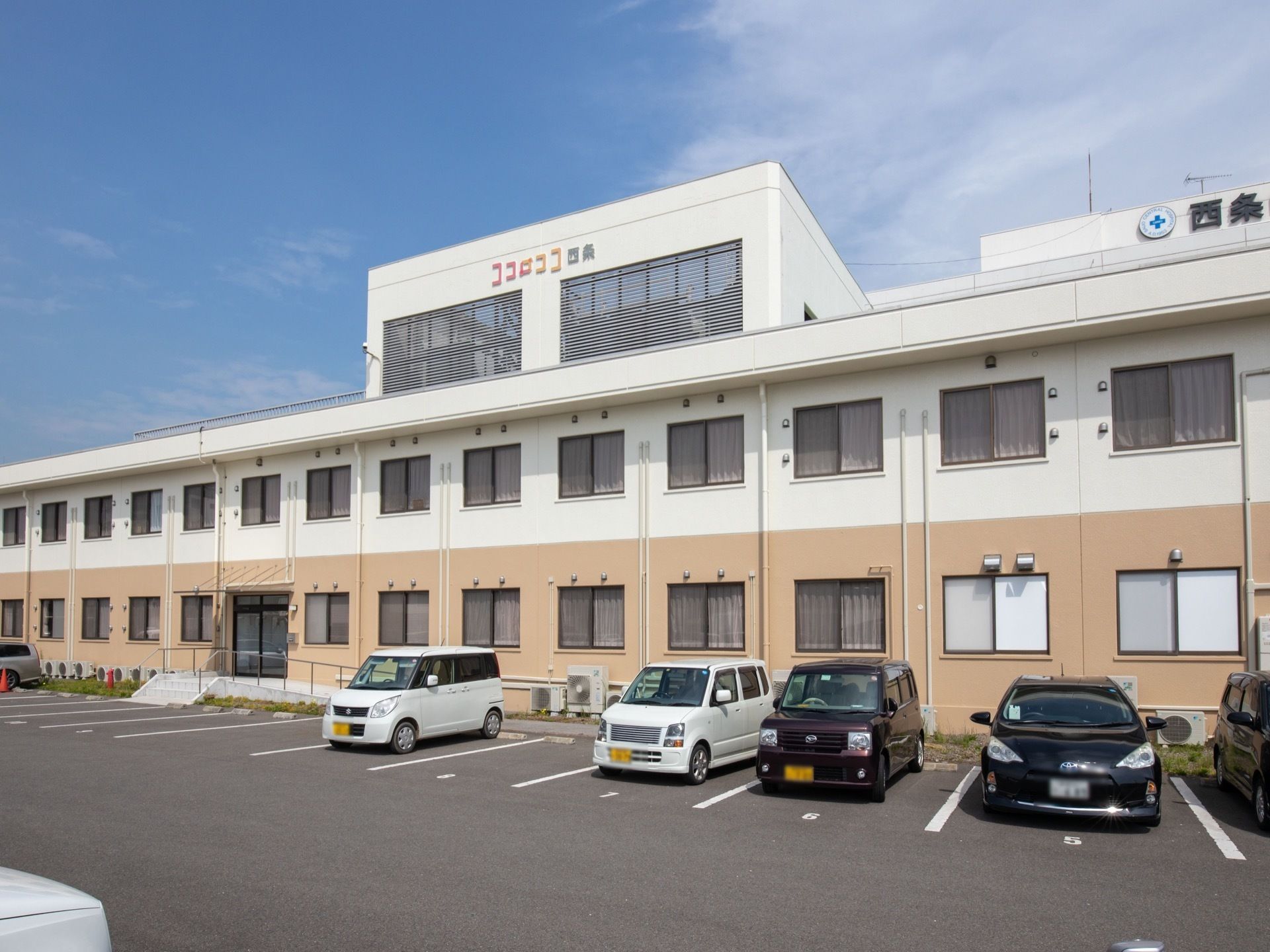 １階部分がベージュ色、２階部分が白色のツートンカラーになっている施設である。敷地内に多くの駐車スペースがある。