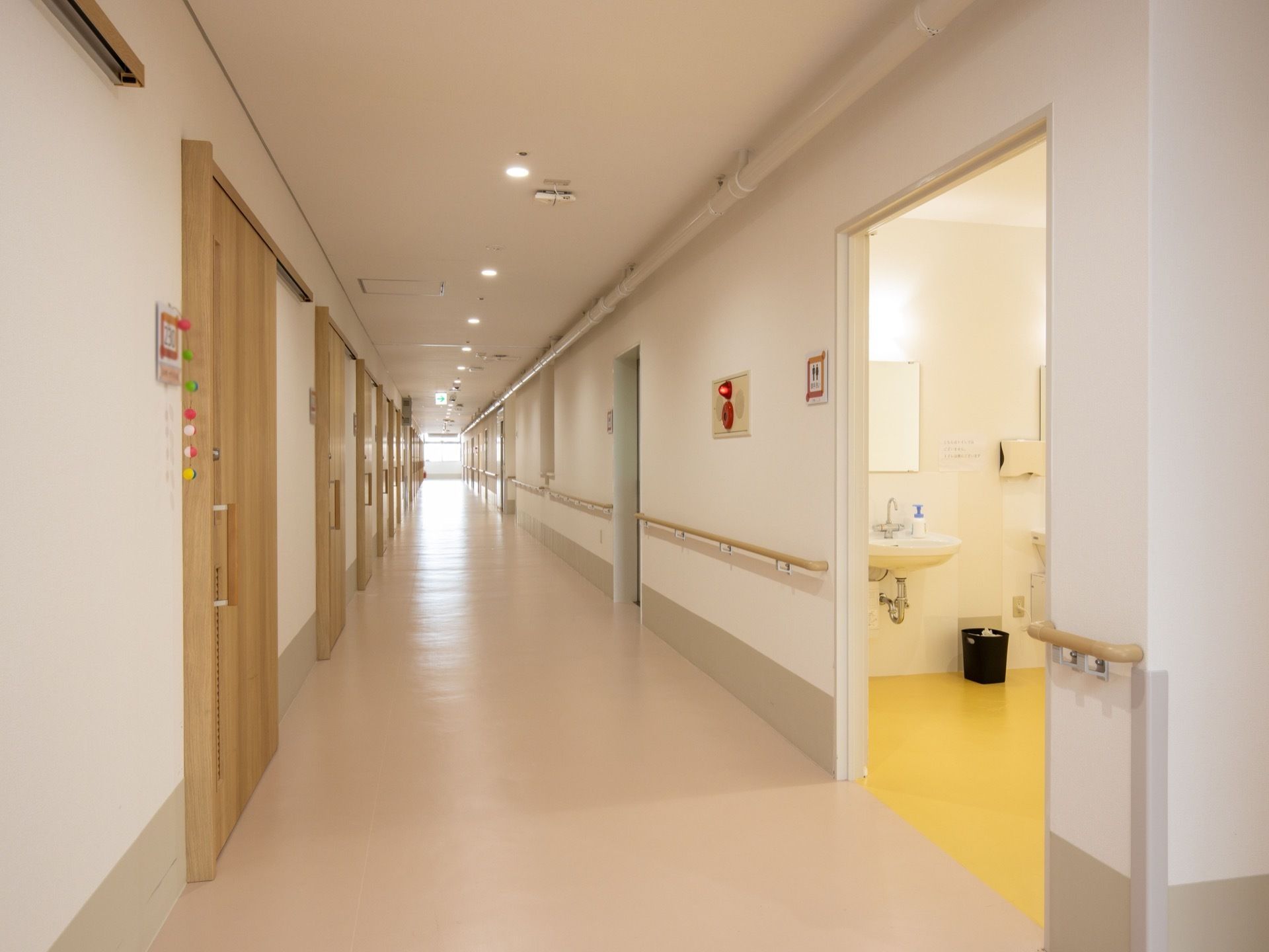 トイレの入口の近くに非常ベルの設備が設置されている。居室入口と反対側の壁に、長い手すりが設置されている。