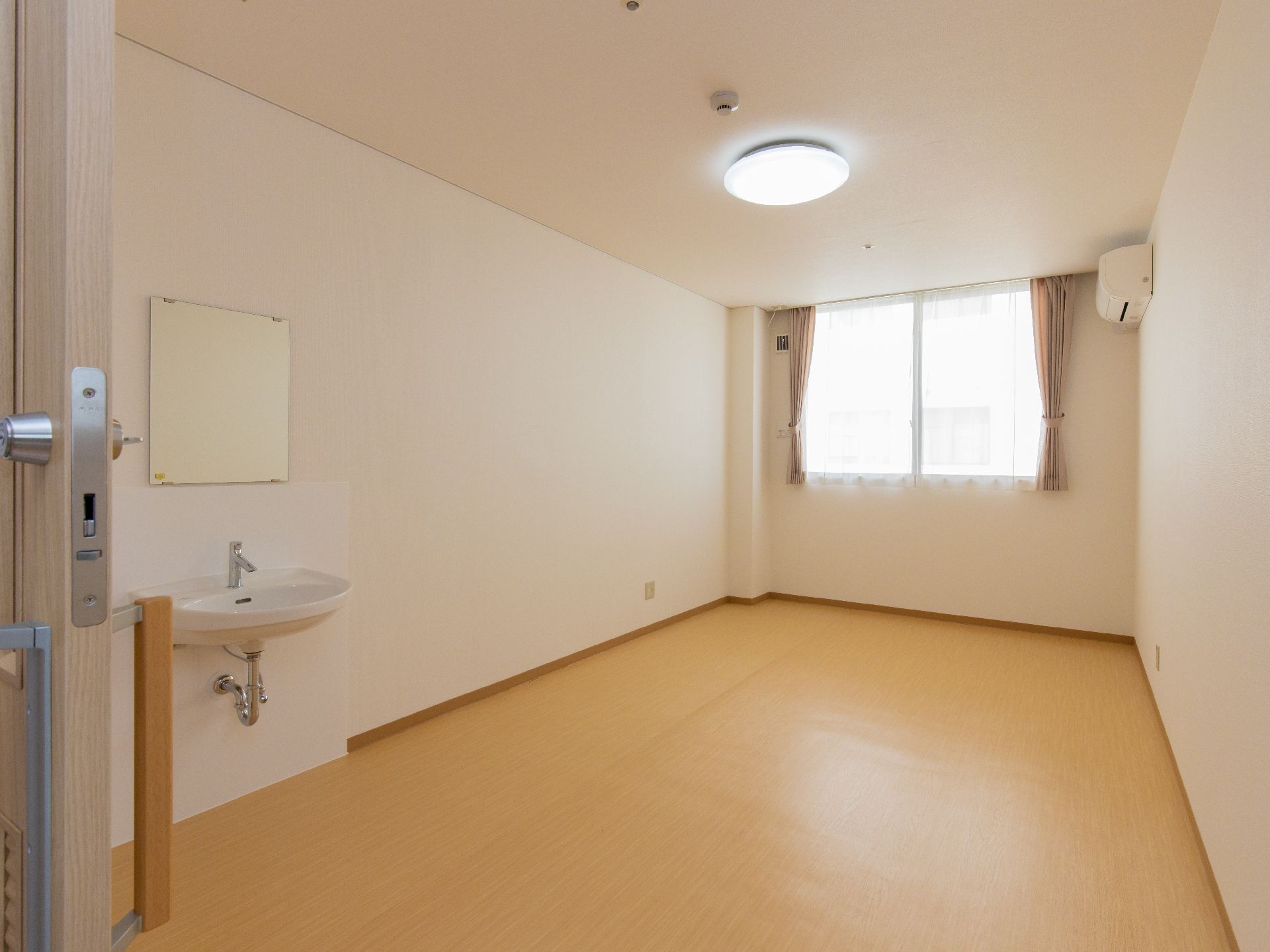 エアコンと鏡付きの手洗い器が備え付けられた個室部屋