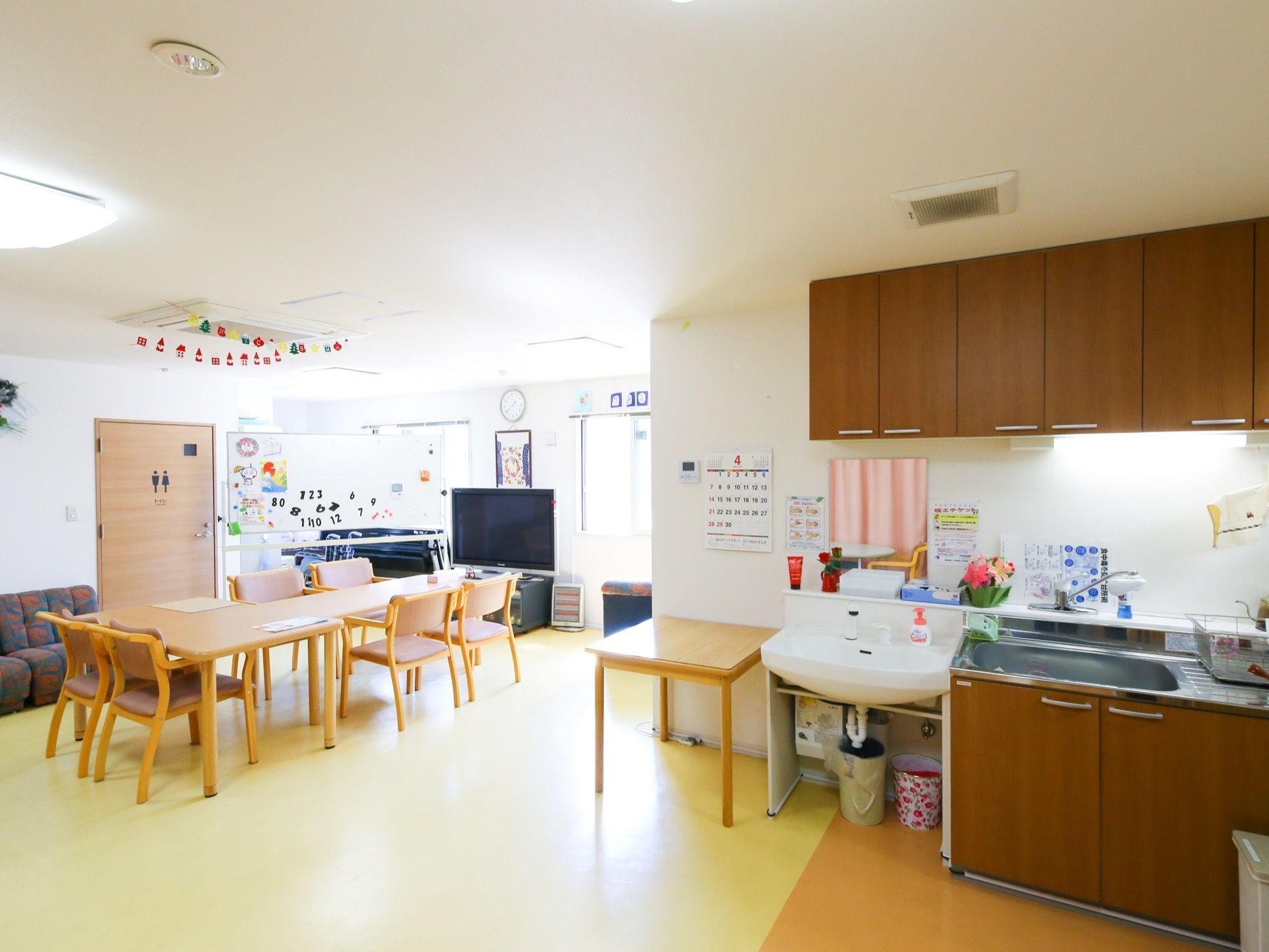 広い共有スペースには木目のシステムキッチンが設置されている。部屋の中ほどにテーブルセットが置かれ、正面にテレビがある。