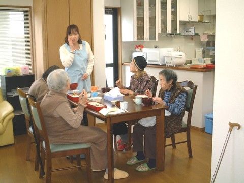 テーブル席で４人の入居者様が食事をする様子を１人の女性スタッフが見守るダイニングキッチン