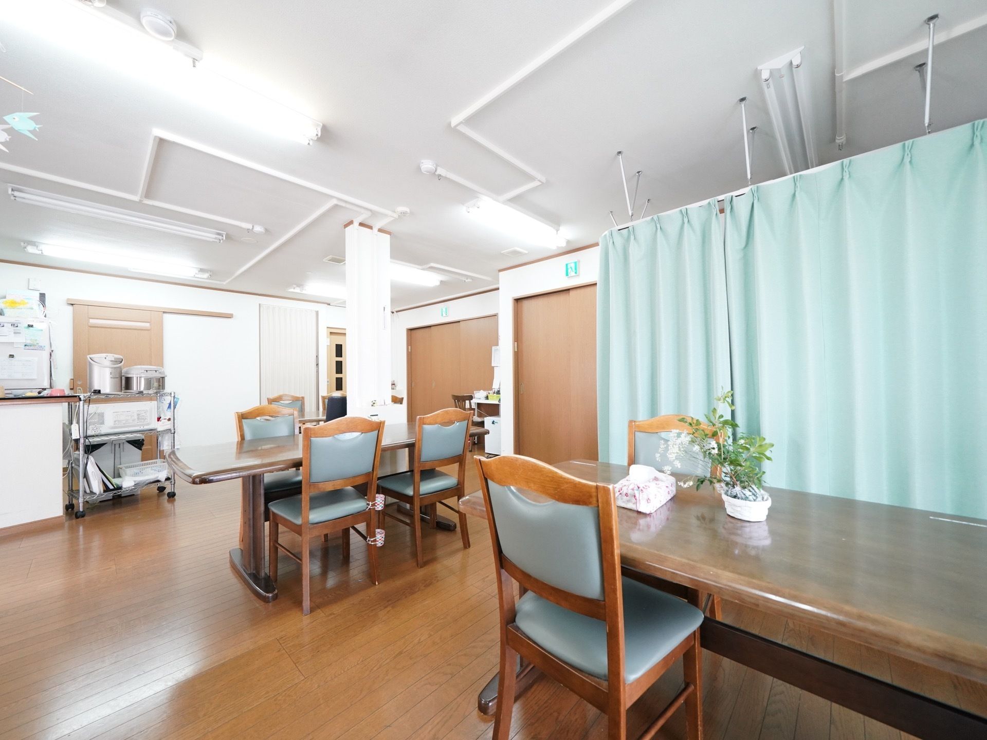 大きな机と椅子が用意され、花などの観葉植物が置かれている。テーブルの後ろには、ブルーのカーテンで仕切られたスペースがある。