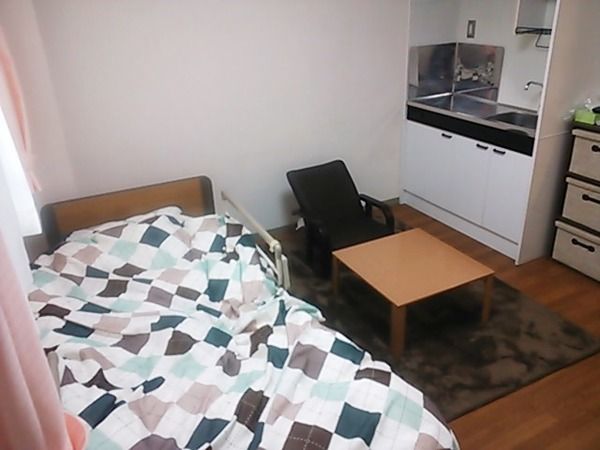 ミニキッチンが付いている施設内の居室の様子。ベッドや座椅子、テーブルがある小さな部屋の様子