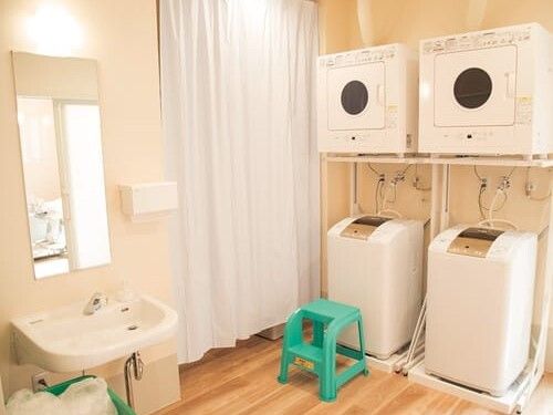 縦型の洗濯機が2台置かれたフローリングの部屋には洗面所もあり、洗濯機の上には乾燥機もある。