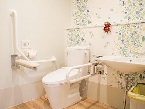 両サイドに手すりがあるトイレは広く、便座の前にはバーが付いている。花柄のクロスが明るい雰囲気。