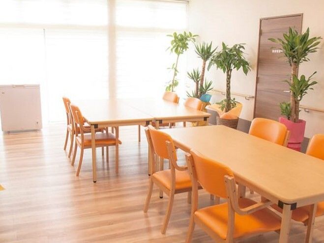 大きな窓があり、明るい雰囲気の食堂にはオレンジの椅子がセットされた木製のテーブルが複数ある。