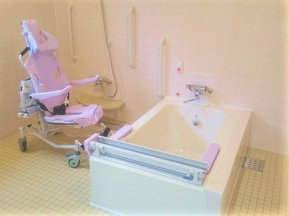 ピンクの浴室用車いすが設置された浴室。浴槽横には呼び出しボタンもついている。
