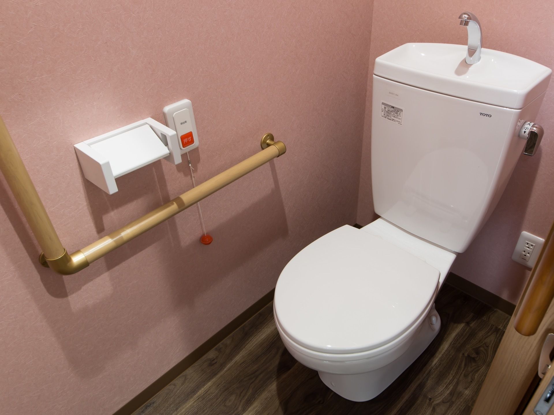 サイドを抑えたピンク色の壁紙が施されたトイレスペースに、洋式便器が据えられている。出入口は間口の広い引き戸である。