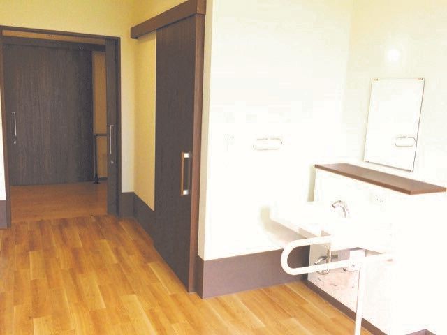 車いす対応の洗面所が付いたフローリングの部屋にはワイドタイプのスライド式のドアが付き、トイレのドアも大きい。家具などはない。