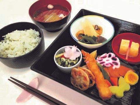 重箱の中に詰められた色鮮やかな料理。レンコンのはさみ揚げや煮物、青菜のおひたし、煮卵など。蝶や花の形に切られた野菜が美しい。