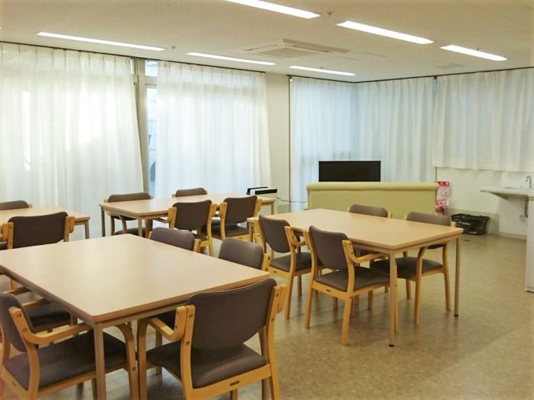 ダイニングテーブルが複数置かれ、奥にはソファやテレビが設置されている。